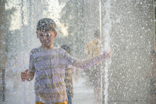 Boy having fun in water fountains. Child playing with a city fountain on hot summer day. Happy kids having fun in fountain. Summer weather. Active leisure, lifestyle and vacation