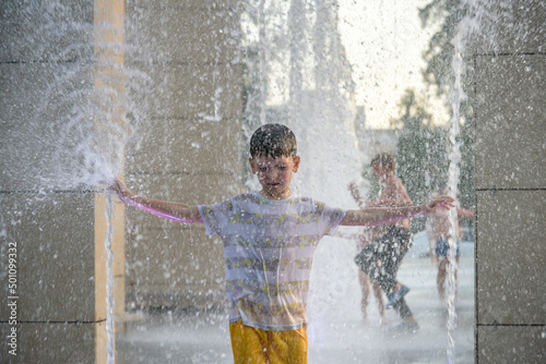 Boy having fun in water fountains. Child playing with a city fountain on hot summer day. Happy kids having fun in fountain. Summer weather. Active leisure  lifestyle and vacation