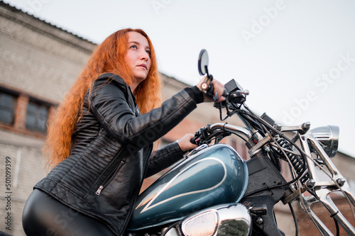 Red-haired curly woman in leather clothing motorcycle outdoors.