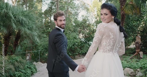 Young married couple walks on path in Isola Del Garda and looks at the camera.