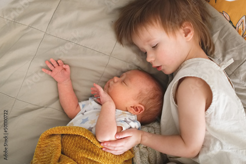Fotografía cute chubby baby sleeps on bed next to an older sibling, children are siblings together