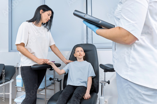 the girl holds her mother's hands and looks frightenedly at nurse photo