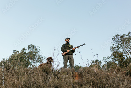 Hunter holding his gun standing smiling looking away in nature