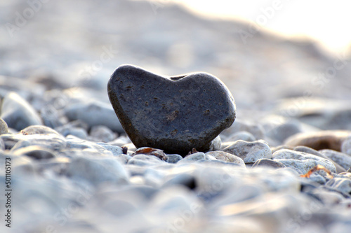Heart shape stone against background of beach. Summer sunny day. Love, wedding and Valentine day concept. Finding beautiful and interesting stones. Beach vacation. 