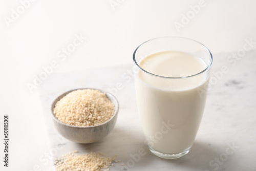 White Sesame milk and bowl with sesame seeds on white background. Close up. Space for text. Healthy lactose free vegetarian beverage.