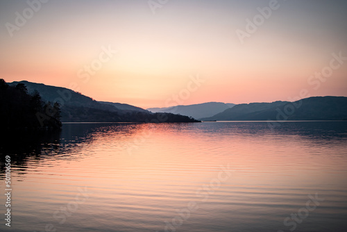 A landscape photograph looking across the waters of Loch Lomond in Scotland at sunset.