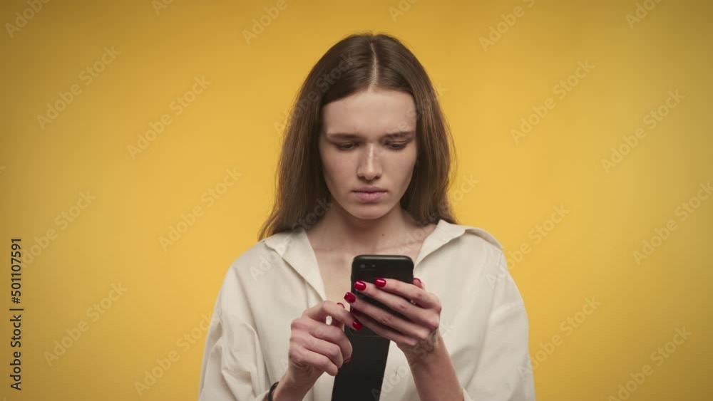 Young adult caucasian woman recieving great news on her smart phone on a bright yellow background Young adult caucasian woman recieving great news on her smart phone on a bright yellow background