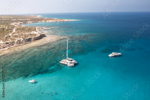 Aerial view of three boats on azure clear water near rocky coast (Cyprus)