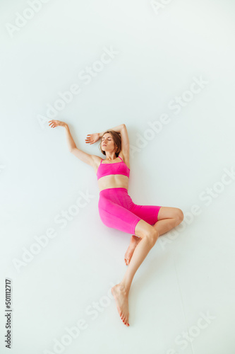 Beautiful sporty blonde woman in pink sportswear lies on a white background. Vertical