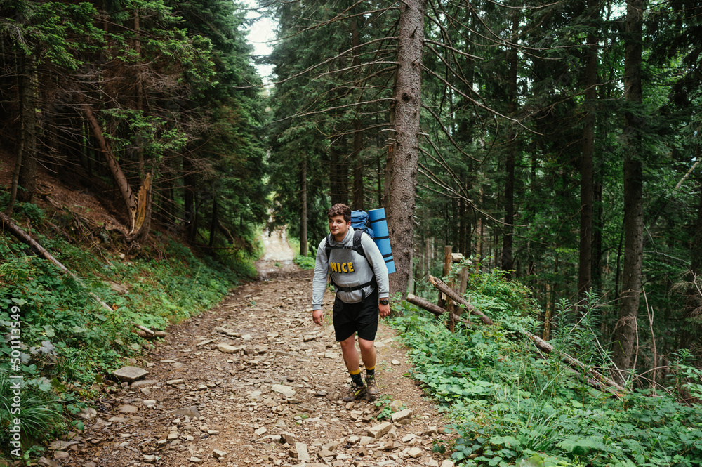 male hiker in casual clothes with a backpack on his back walks on a trail in the mountains during a hike.