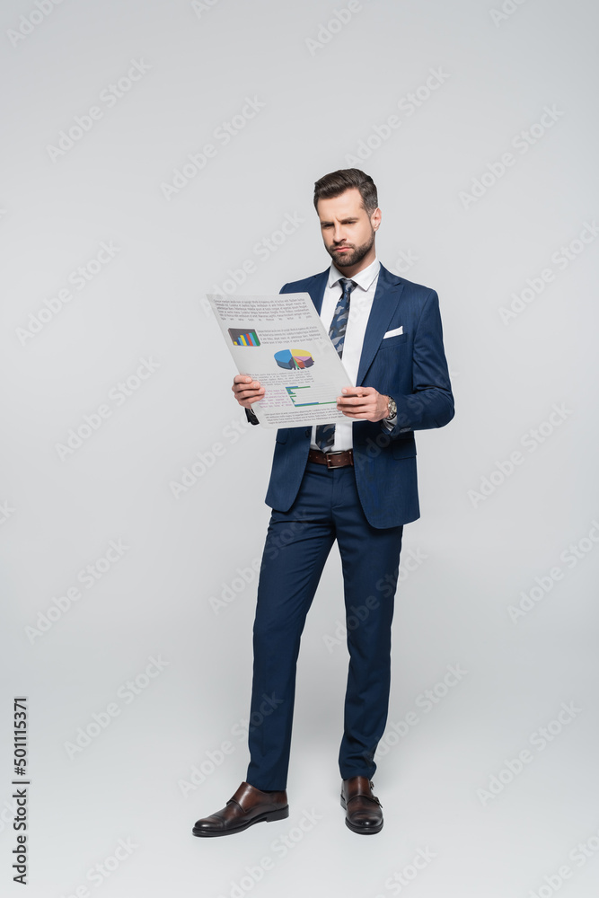 full length view of economist reading document with analytics on grey. full length view of economist reading document with analytics on grey.