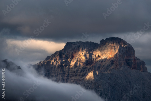 Sunset on Croda Rossa d'Ampezzo mountains surrounded by the fog and darkness with only a few spots of sun light, Dolomites, Veneto photo