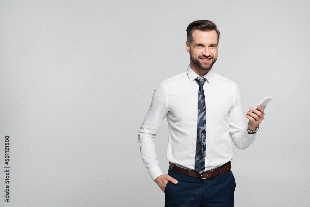 cheerful businessman holding hand in pocket and mobile phone isolated on grey. cheerful businessman holding hand in pocket and mobile phone isolated on grey.