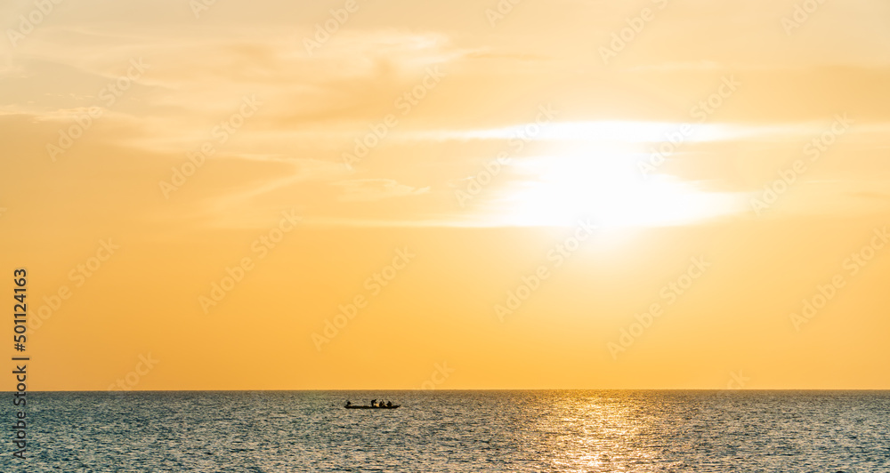 Sunset sky over sea in the evening with orange sunlight and minimal fishing boat