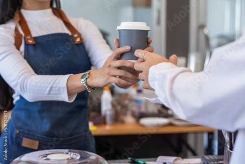 young barista delivers hot coffee in take away paper cup to customer before making payment at counter. cashier is delivering  hot cup of coffee to customer after completing the check at counter.