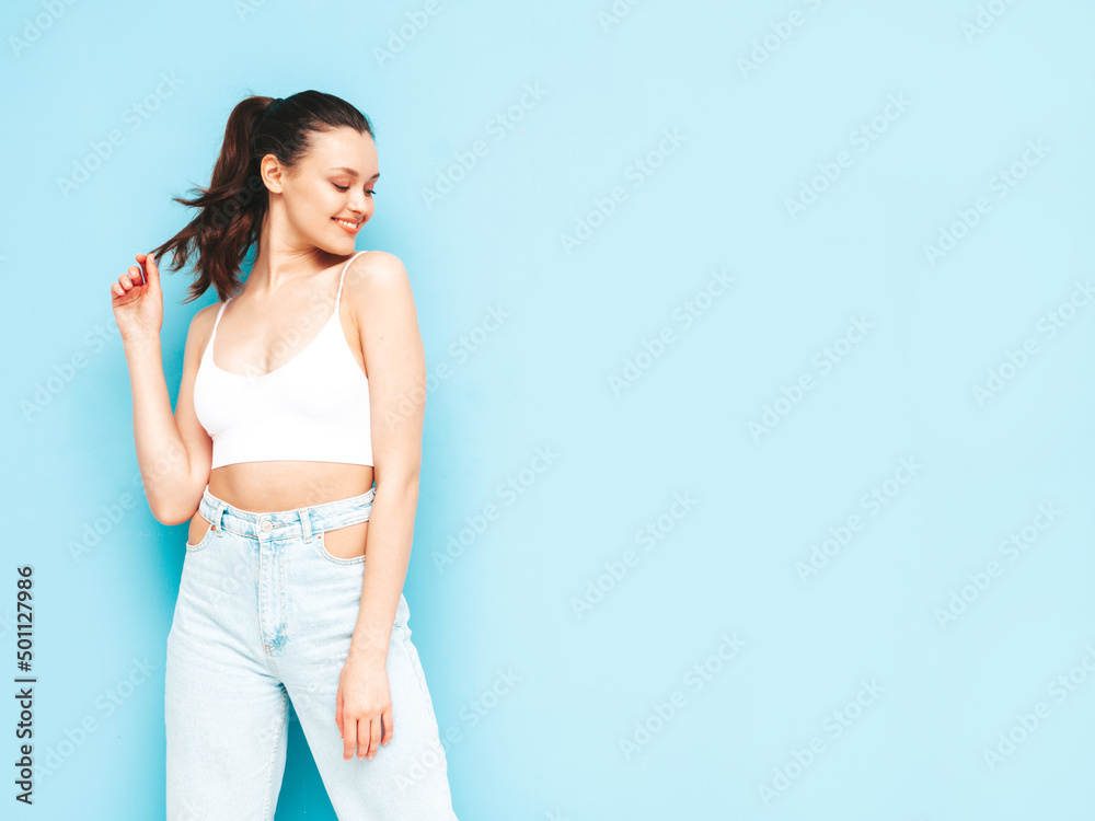 Young beautiful smiling female in trendy summer jeans and top clothes. Sexy carefree woman posing near blue wall in studio. Positive brunette model having fun.Cheerful and happy Young beautiful smiling female in trendy summer jeans and top clothes. Sexy carefree woman posing near blue wall in studio. Positive brunette model having fun.Cheerful and happy