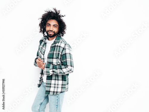Handsome smiling hipster model.Sexy unshaven Arabian man dressed in summer shirt and jeans clothes. Fashion male with long curly hairstyle posing near wall in studio. Isolated on white