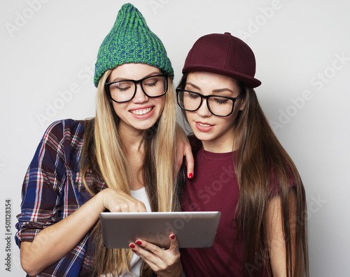 two hipster female friends use digital tablet, studio shot over gray vackground photo