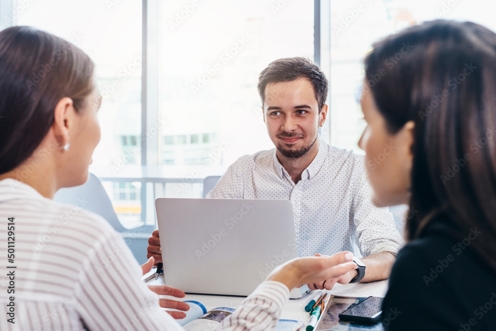 Man sits across from two women at desk in office and listens to them.