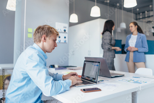 Man works with laptop in office next to his colleagues talking