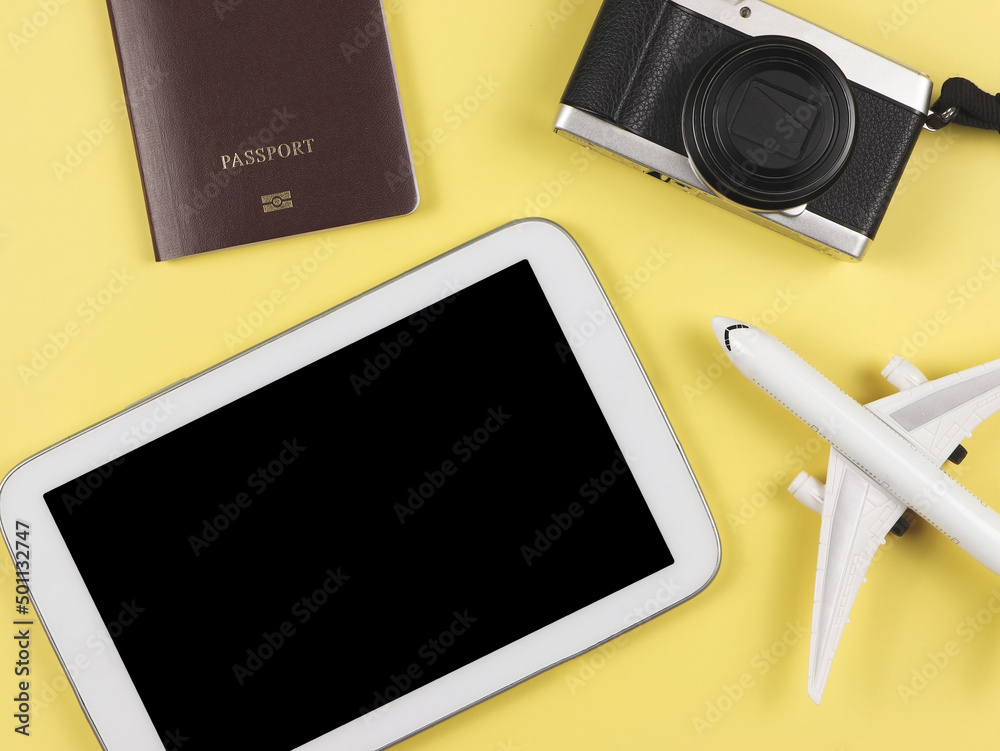 flat lay of passport, camera and airplane model and digital tablet with blank black screen on yellow background. flat lay of passport, camera and airplane model and digital tablet with blank black screen on yellow background.