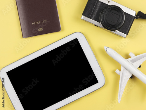flat lay of passport, camera and airplane model and digital tablet with blank black screen on yellow background.