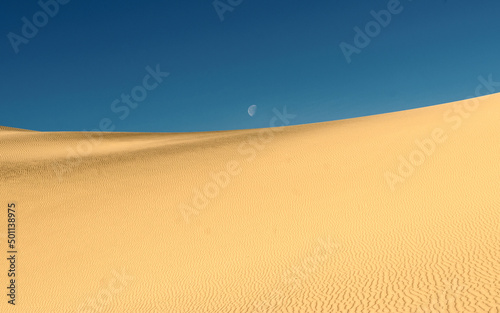 Moon against blue sky over sand dunes. Sand dunes against the blue sky.