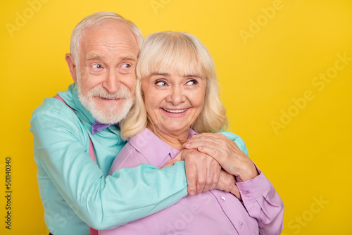 Portrait of two attractive cheerful amorous tender grey-haired spouses bonding isolated over bright yellow color background