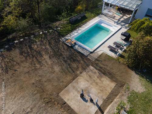 Drone flight over fresh earth area with grass grown next to pool construction site in April