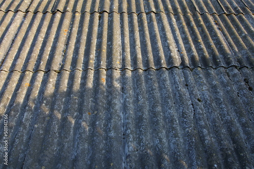 Old asbestos roofing sheets on the roof. Corrugated panels, grey slate texture, wavy roof background.