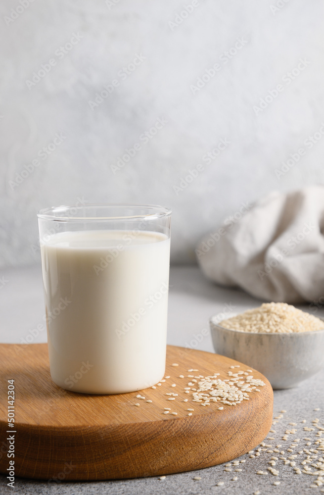Sesame milk in glass and white sesame seeds in bowl on light background. Vegan plant based milk replacer. Vertical orientation. Close up. Sesame milk in glass and white sesame seeds in bowl on light background. Vegan plant based milk replacer. Vertical orientation. Close up.