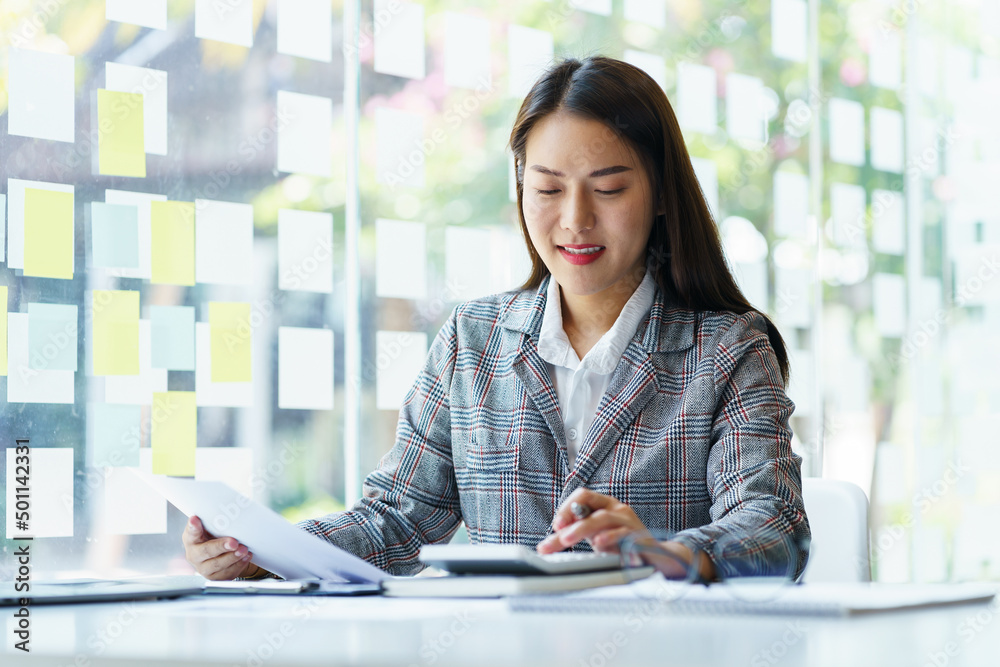 Happy Asian Business woman using calculator for doing math finance on a wooden desk, tax, accounting, statistics and holding paper chart of accounting. Happy Asian Business woman using calculator for doing math finance on a wooden desk, tax, accounting, statistics and holding paper chart of accounting.