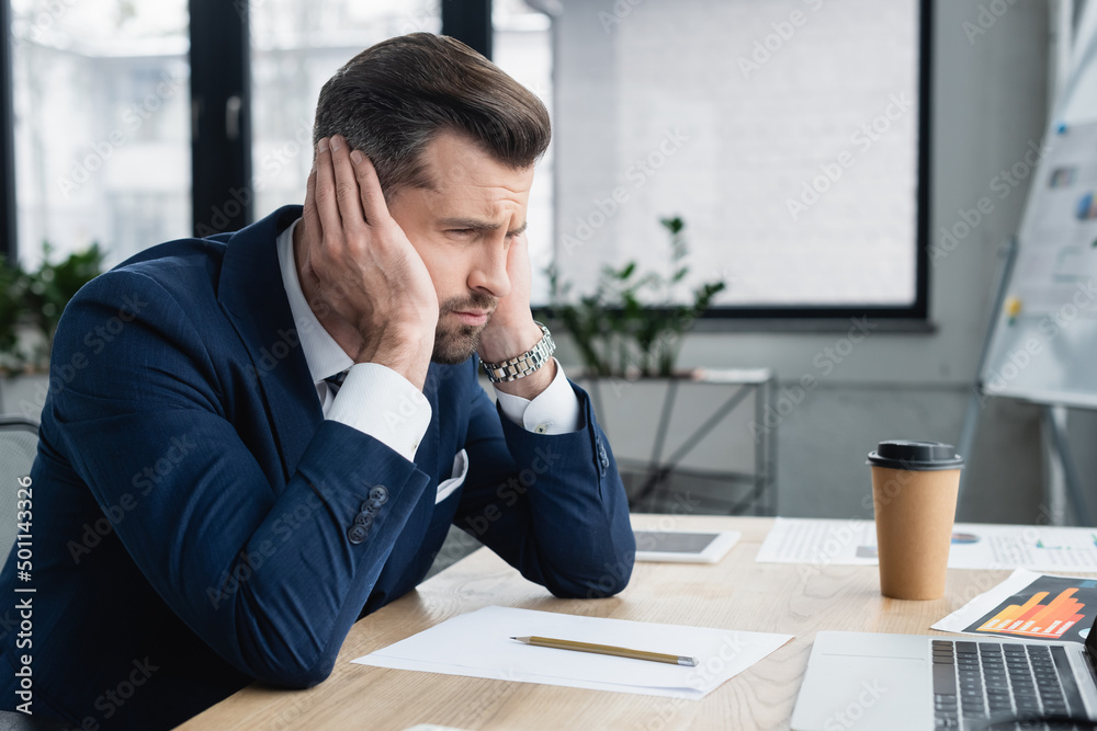 upset economist sitting at workplace near papers and coffee to go. upset economist sitting at workplace near papers and coffee to go.