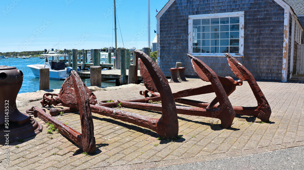 Old rusted anchors in display in front of an old wooden building in