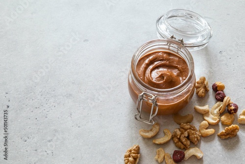 Walnut, hazelnut and cashew nut butter in glass jar on light background. Homemade raw organic mixed nuts spread. Healthy natural food concept. Copy space. Selective focus.
