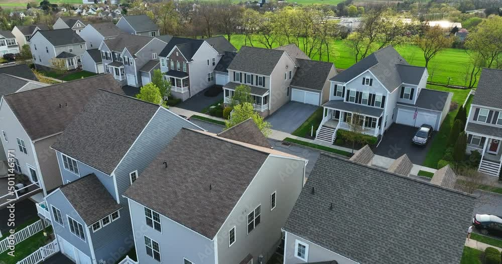 Street with new homes in spring season. Single family houses and residential construction in USA planned community. Aerial from backyard to front exterior reveal as car drives by.