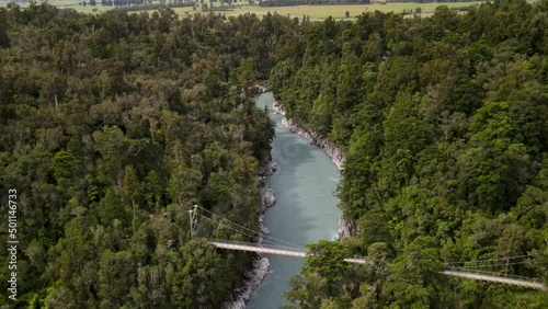 Turquoise and green water in Hokitika Gorge surrounded by lush native forest - aerial reveal of suspension bridge and New Zealand landscape. photo