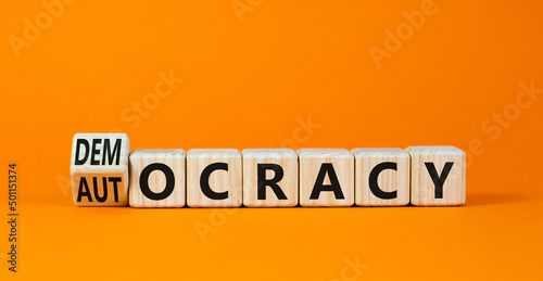 Democracy or autocracy symbol. Turned wooden cubes and changed the concept word Autocracy to Democracy. Beautiful orange background. Copy space. Business democracy or autocracy concept.