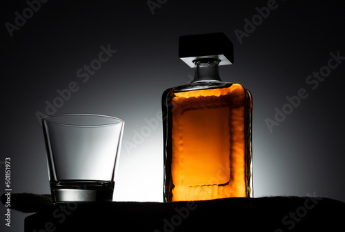 Empty glass and bottle of whiskey on black background and backlight