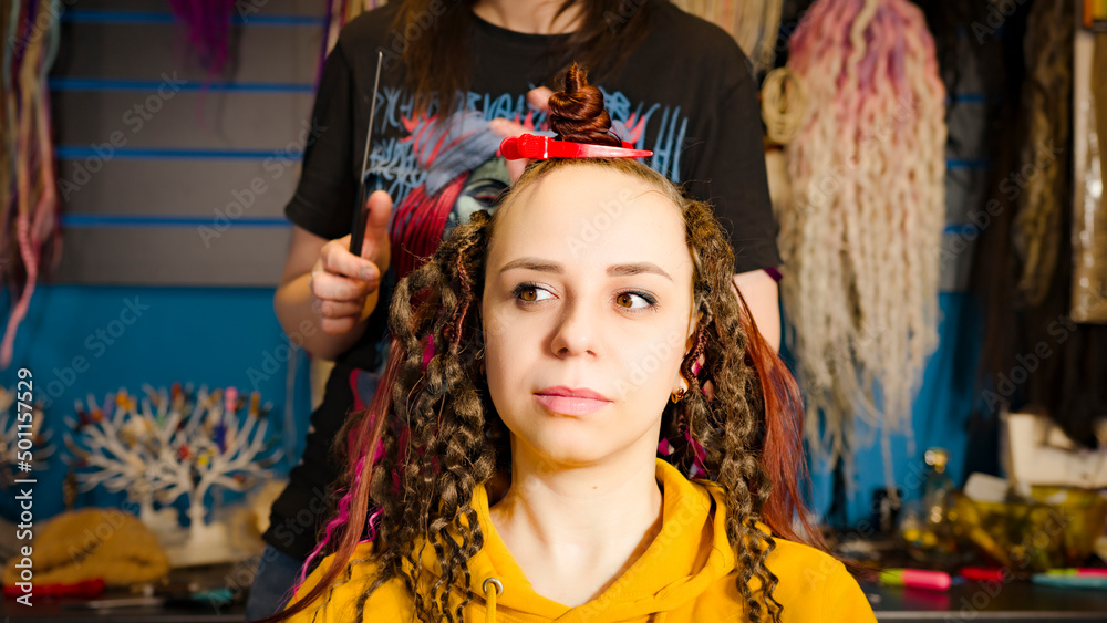 Unrecognizable person makes hairstyle for young woman in salon. Professional hairstylist makes hairdo for client.