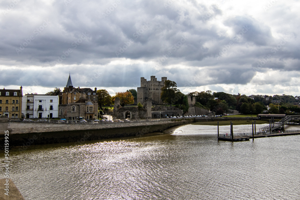 Rochester Castle, from the bridge across the Medway River.  Storm clouds were gathering but the sun was still shining.  Sunbeams are seen through the clouds.  October 2021.