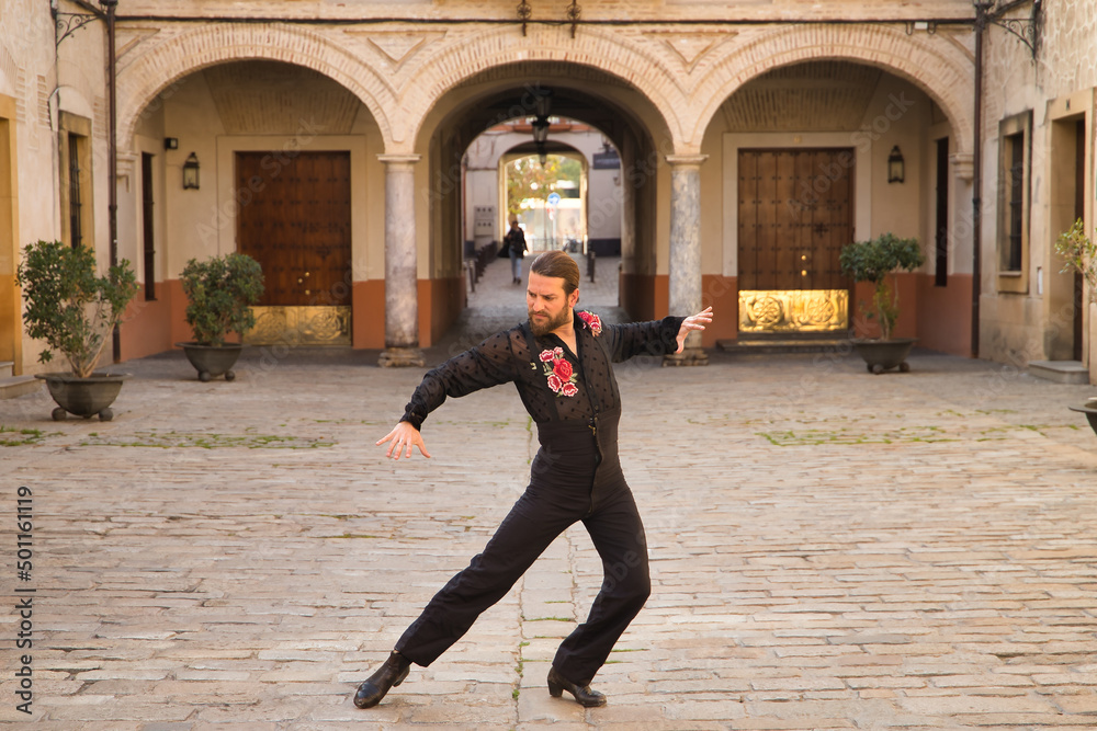 Young man with beard and ponytail, wearing black transparent shirt with black polka dots and red roses, black pants and jacket, dancing flamenco in the city. Concept art, dance, culture, tradition. Young man with beard and ponytail, wearing black transparent shirt with black polka dots and red roses, black pants and jacket, dancing flamenco in the city. Concept art, dance, culture, tradition.