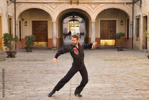 Young man with beard and ponytail, wearing black transparent shirt with black polka dots and red roses, black pants and jacket, dancing flamenco in the city. Concept art, dance, culture, tradition.