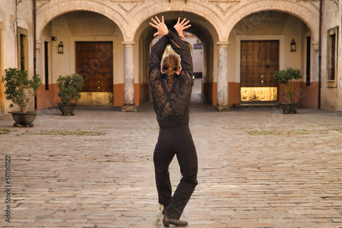 Young man with beard and ponytail, wearing black transparent shirt with black polka dots, black pants and jacket, dancing flamenco in the city. Concept art, dance, culture, tradition.