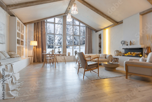 cozy warm home interior of a chic country chalet with a huge panoramic window overlooking the winter forest. open plan, wood decoration, warm colors and a family hearth photo