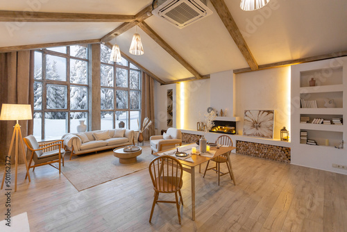 cozy warm home interior of a chic country chalet with a huge panoramic window overlooking the winter forest. open plan, wood decoration, warm colors and a family hearth photo