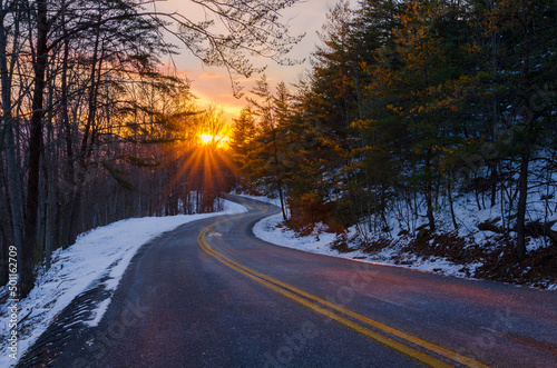 Rural road trailing off into the sunset with snow on the ground