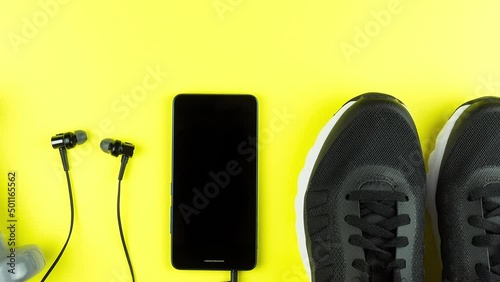 Fitness equipment. Sneakers, water, dumbbells and headphones on yellow background