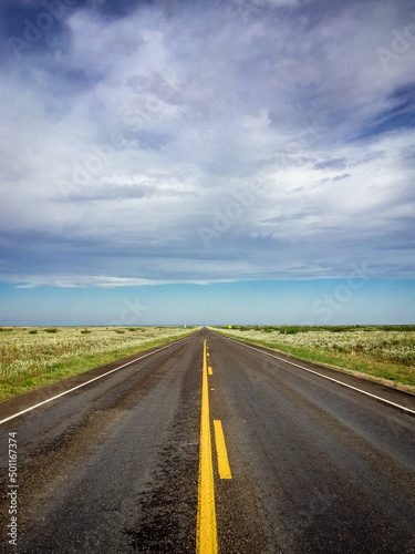 Blacktop Road View to Vanishing Point on the Horizon under a Cloudy Blue Sky in the Country © Carrie