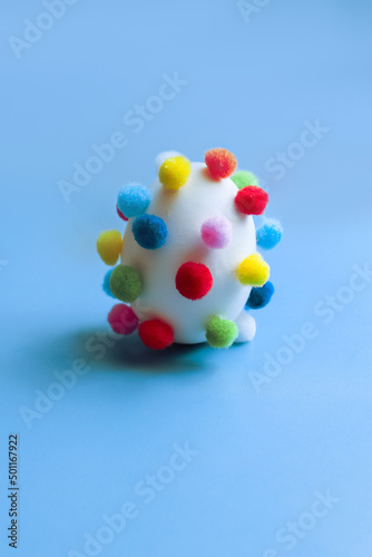 Egg covered with pom-poms on a blue background  funny egg